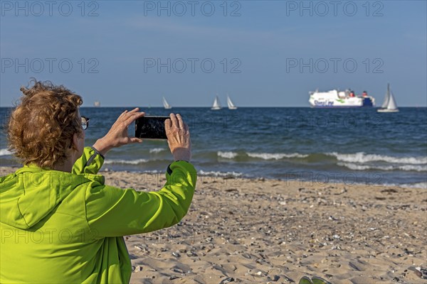 Older woman taking photos of boats, sailing boats, ferry, smartphone, Kieler Woche, Falckensteiner Strand, Kiel Fjord, Kiel, Schleswig-Holstein, Germany, Europe