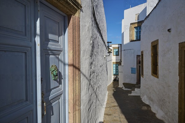 A narrow alley with white buildings, blue doors and wooden windows under a clear blue sky, Chora, main town of Patmos, Patmos, Old Town, Dodecanese, Greek Islands, Greece, Europe