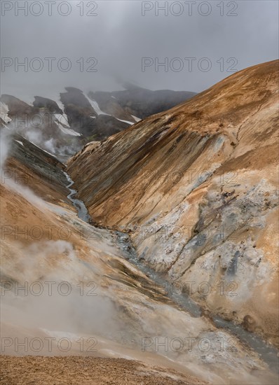 Steaming stream between colourful rhyolite mountains and snowfields, Hveradalir geothermal area, Kerlingarfjöll, Icelandic Highlands, Iceland, Europe