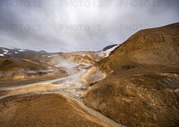 Steaming stream between colourful rhyolite mountains with snowfields, Hveradalir geothermal area, Kerlingarfjöll, Icelandic highlands, Iceland, Europe