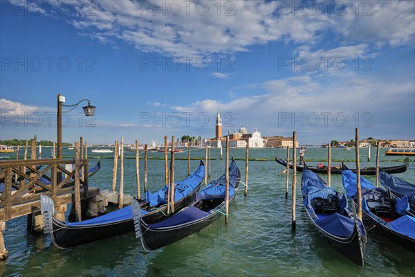 VENICE, ITALY, JUNE 27, 2018: Gondolas and gondolier in lagoon of Venice by Saint Mark (San Marco) square with San Giorgio di Maggiore church in background in Venice, Italy, Europe