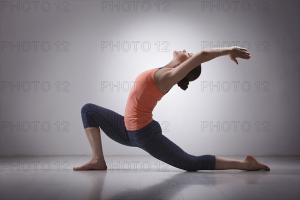 Beautiful sporty fit yogini woman practices yoga asana Anjaneyasana, low crescent lunge pose in surya namaskar in studio