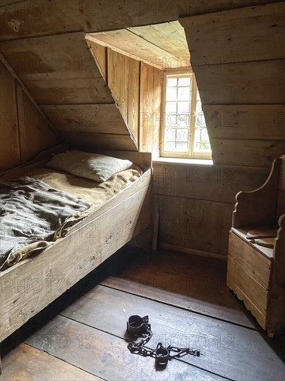 Prison cell in historic rebuilt town hall with left bed with bed linen bedding of coarse linen in the foreground on the floor handcuffs footcuffs right chair toilet chair with privy toilet outhouse in old rebuilt schoolhouse and town hall from 1830 in Open Air Museum Neuhausen, Neuhausen ob Eck, district Tuttlingen, Baden-Württemberg, Germany, Europe