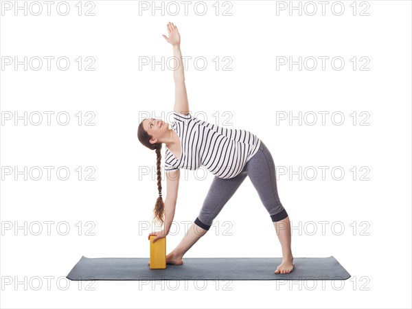 Pregnancy yoga exercise, pregnant woman doing asana Utthita trikonasana, extended triangle pose with block isolated on white background