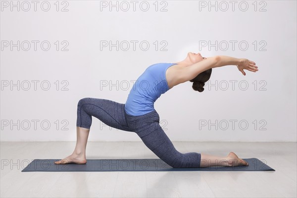 Beautiful sporty fit yogini woman practices yoga asana Anjaneyasana, low crescent lunge pose in surya namaskar in studio