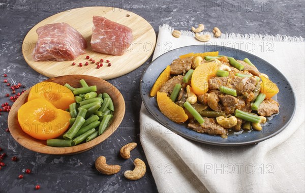 Fried pork with peaches, cashew and green beans on a black concrete background. side view, close up, chinese cuisine. linen textile