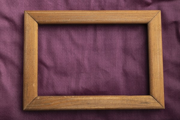 Wooden frame on smooth cotton purple tissue. Top view, flat lay, natural textile background and texture