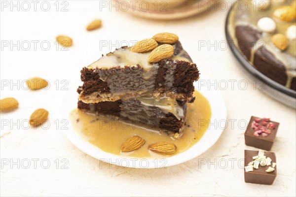 Pieces of chocolate brownie cake with caramel cream and almonds on a white concrete background. Side view, close up, selective focus