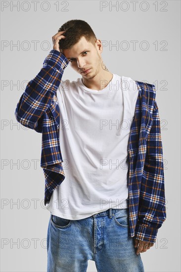 Young cocky man in checkered shirt and jeans touching his head