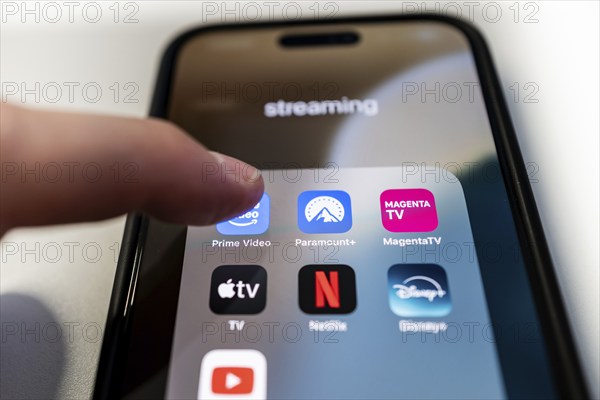 One finger touches the Prime Video app icon on a smartphone screen with various other streaming apps