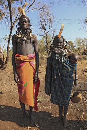 Southern Ethiopia, in Maco National Park, Mursi tribe, Mursi man, Mursi woman with baby, painted skin and headdress, plate-lipped woman, woman with plate in lower lip, Ethiopia, Africa