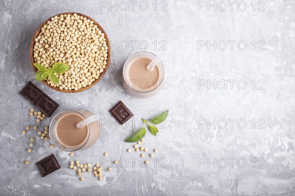 Organic non dairy soy chocolate milk in glass and wooden plate with soybeans on a gray concrete background. Vegan healthy food concept, flat lay, top view, copy space