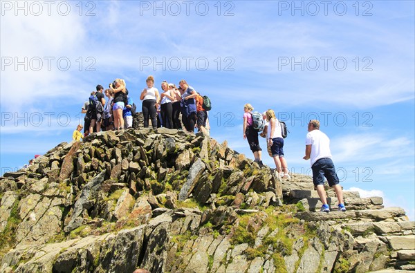 Walkers crowd onto the summit point, Mount Snowdon, Gwynedd, Snowdonia, north Wales, UK