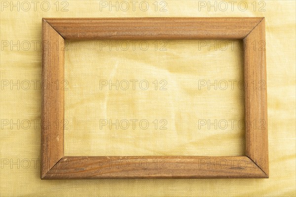 Wooden frame on smooth yellow linen tissue. Top view, flat lay, natural textile background and texture