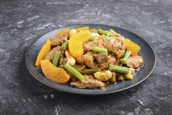 Fried pork with peaches, cashew and green beans on a black concrete background. Side view, close up, chinese cuisine