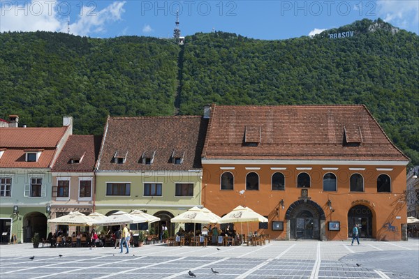 A lively town square in front of historic buildings with cafés at the foot of a green mountain, town houses on the market square Piata Sfatului, Old Town and Tâmpa Mountain, Brasov, Brasov, Transylvania, Romania, Europe