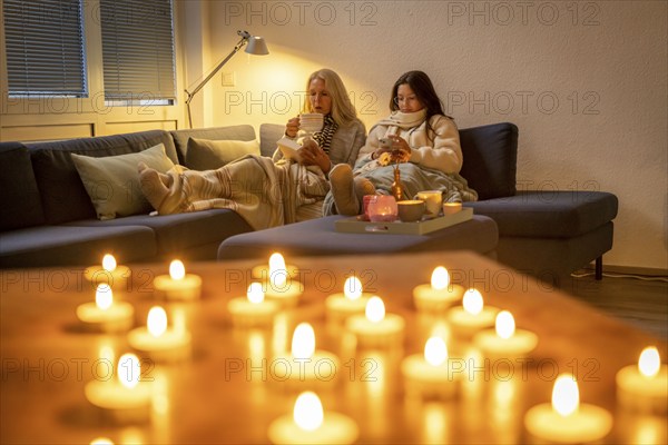 Symbolic image energy saving, cold winter, energy crisis, cold flat, mother and daughter lying on the sofa, warmly dressed, candlelight, heating on to a minimum