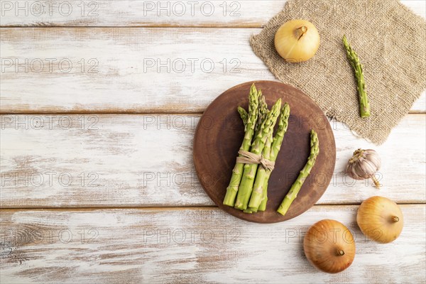 Bunch of fresh green asparagus, garlic, onion on white wooden background. Top view, flat lay, copy space. harvest, healthy, vegan food, concept