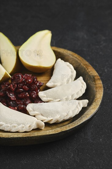 Close-up view of empanadas on a wooden platter, accompanied by a serving of sweet cranberries and two slices of juicy pear. This appetizing display combines textures and flavors.