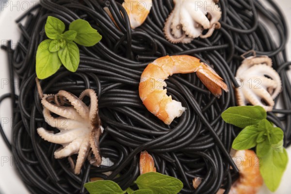 Black cuttlefish ink pasta with shrimps or prawns and small octopuses on gray wooden background and blue textile. Top view, close up, selective focus