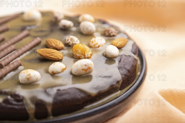 Homemade chocolate brownie cake with caramel cream and almonds with cup of coffee on a white concrete background and orange textile. Side view, close up, selective focus