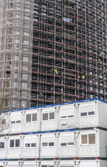 Large construction site, construction of a high-rise residential building, scaffolded shell, already fitted with windows, in front of it containers for offices, accommodation, washrooms, storage, for the construction workers