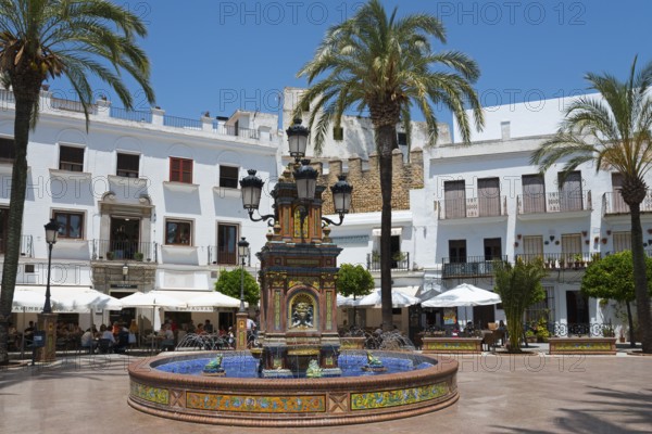 A central fountain in a sunny plaza surrounded by white buildings and palm trees, fountain with azulejos, Plaza de España, square, old town, Vejer de la Frontera, Cadiz province, Cadiz, Andalusia, Spain, Europe