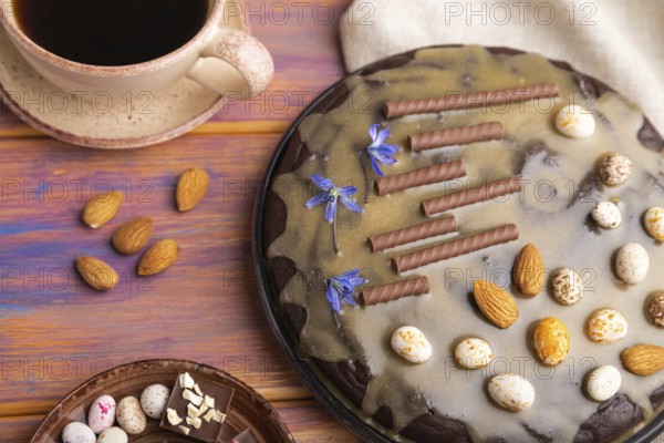 Homemade chocolate brownie cake with caramel cream and almonds with cup of coffee on a colored wooden background and linen textile. Top view, close up, selective focus