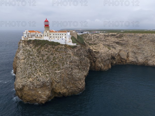 A red lighthouse and white buildings stand on an imposing cliff with a wide view of the ocean, aerial view, lighthouse, Cabo de São Vicente, Cape St Vincent, Cape St Vincent, Sagres, Portugal, Europe