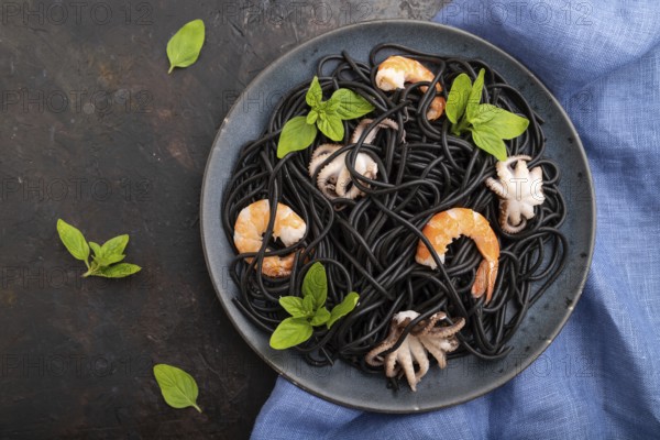 Black cuttlefish ink pasta with shrimps or prawns and small octopuses on black concrete background and blue textile. Top view, flat lay, close up