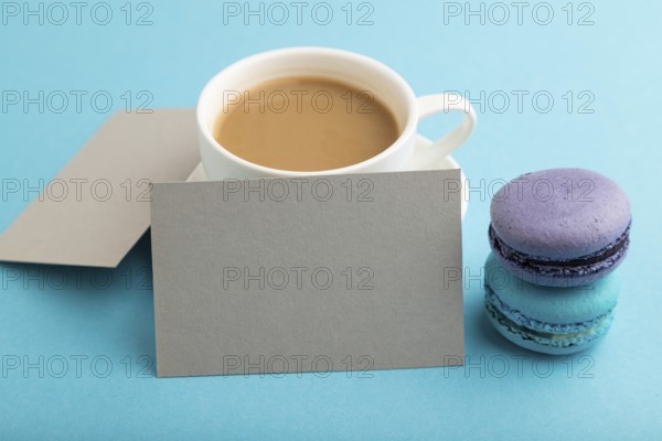 Gray paper business card mockup with blue and violet macaroons and cup of coffee on blue pastel background. Blank, side view, copy space, still life, close up. morning, breakfast concept