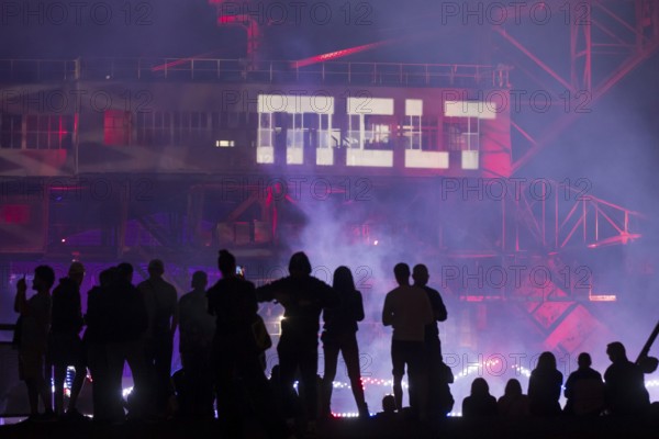 A silhouette of several festival visitors in front of the logo projected onto an excavator at the Melt Festival in Ferropolis on 13 July 2024. After a total of 27 years, the festival will take place for the last time in 2024