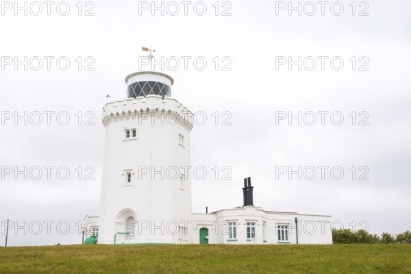 A white lighthouse stands in front of an overcast sky on a green meadow, South Foreland Lighthouse, White cliffs of Dover, Kent, England, Great Britain