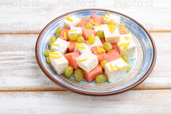 Vegetarian salad with watermelon, feta cheese, and grapes on blue ceramic plate on white wooden background. Side view, close up