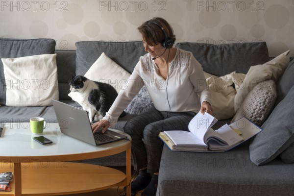 Woman, mid-50s, works from home, with laptop and communicates with colleagues via headset, home office, on the sofa