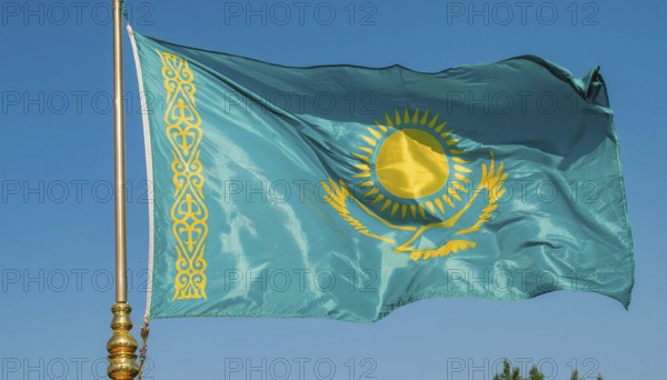 The flag of Kazakhstan flutters in the wind, isolated against a blue sky