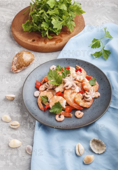 Boiled shrimps or prawns and small octopuses with herbs on a blue ceramic plate on a gray concrete background and blue textile. Side view, close up