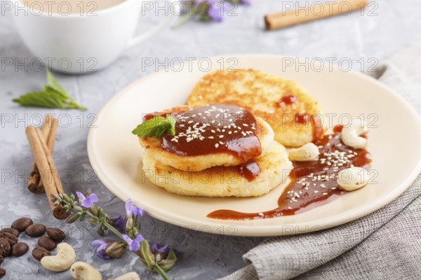 Cheese pancakes with caramel sauce on a beige ceramic plate and a cup of coffee on a gray concrete background. side view, close up