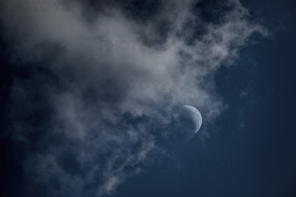 The crescent of the waxing moon in the second quarter shines in a cloudy, dark blue sky, fairytale-like, mystical night shot, dark, somewhat spooky mood, ghostly, symbolic image for fear, fantasy, Lower Saxony, Germany, Europe