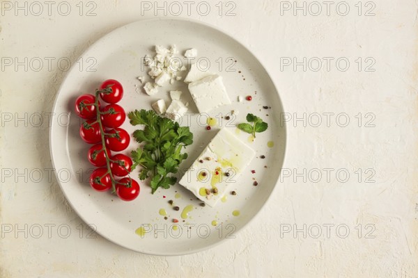 Feta cheese, for salads, with cherry, green butter, greens, on a white plate, appetizer, top view, close-up