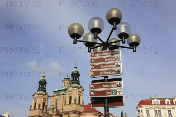 A street lamp on the Old Town Square with signs of the sights in the city and the towers of the baroque St Nicholas Church, Prague, Czech Republic, Europe