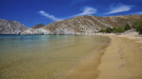 Extensive golden sandy beach with clear water, framed by rocks and trees under a bright blue sky, Psili Ammos Srand, Patmos, Dodecanese, Greek Islands, Greece, Europe