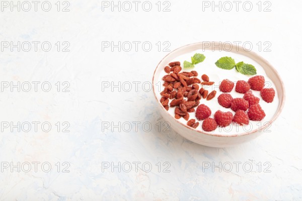 Yogurt with raspberry and goji berries in ceramic bowl on white concrete background. Side view, copy space, close up