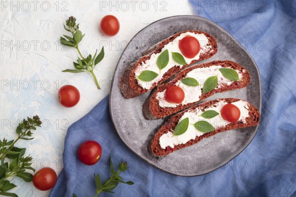 Red beet bread sandwiches with cream cheese and tomatoes on white concrete background and blue linen textile. top view, flat lay, close up