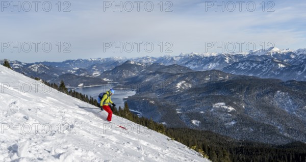 Skiers skiing down the Simetsberg, view of Walchensee and mountain panorama, Estergebirge, Bavarian Prealps, Bavaria Germany