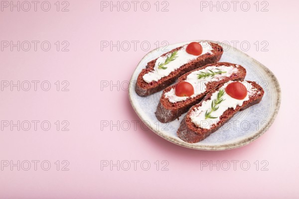 Red beet bread sandwiches with cream cheese and tomatoes on pastel pink background. Side view, copy space