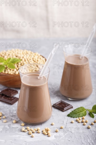 Organic non dairy soy chocolate milk in glass and wooden plate with soybeans on a gray concrete background. Vegan healthy food concept, close up, side view