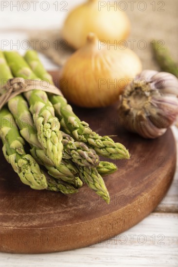 Bunch of fresh green asparagus, garlic, onion on white wooden background. Side view, selective focus. harvest, healthy, vegan food, concept