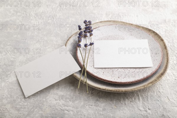 White paper invitation card, mockup with lavender on ceramic plate and gray concrete background. Blank, side view, still life, copy space