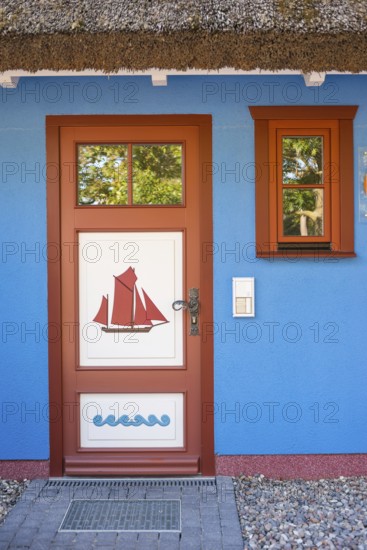 Colourful front door in brown, white and blue with a sailing ship as a motif and matching window frames in the blue wall of a thatched house, thatched roof, historic wooden door with carvings, maritime, artists' village Baltic resort Ahrenshoop, Fischland, Fischland-Darß-Zingst peninsula, Baltic Sea, Mecklenburg-Western Pomerania, Germany, Europe